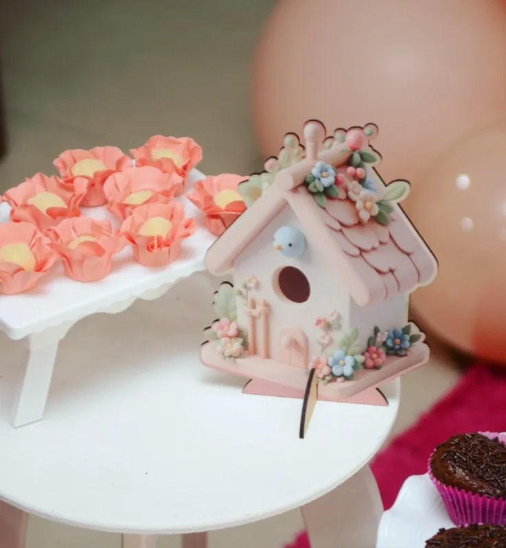 Casinha de passarinho decorativa com flores ao lado de docinhos em forminhas de pétala